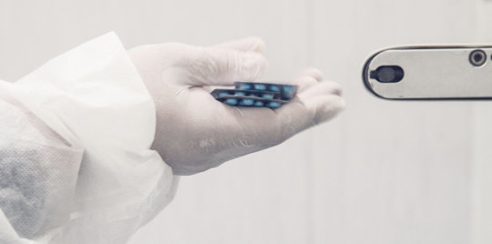 Scientist holding some pills, wearing gloves.