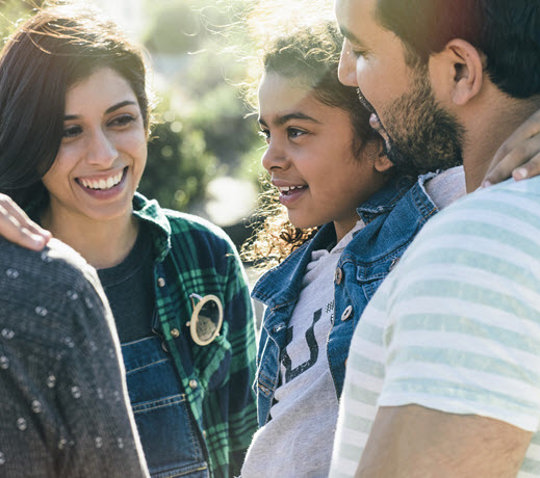 Family of four sitting together, smiling warmly, with a simple background highlighting their joy and togetherness.