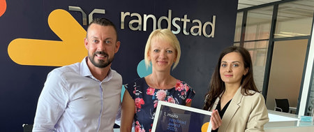 Three people smiling, holding the reward for first place at Randstad.