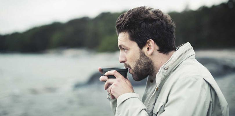 Man drinking from a mug at the beach.